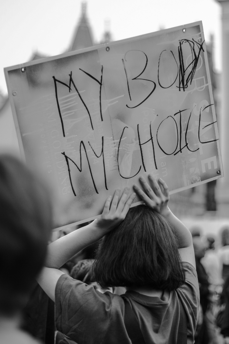 black and white image of a woman holding a protest sign declaring my body my choice. 
